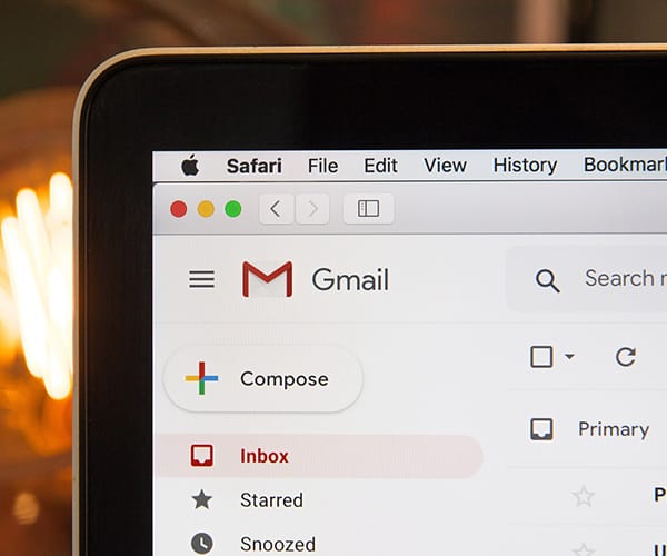 A close-up shot of a corner of a MacBook displaying the Gmail logo.